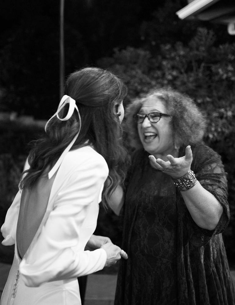 An expressive Mitzi Schwarz, congratulates a bride, whose back is to the camera. Mitzi Schwarz - Wedding Officiant